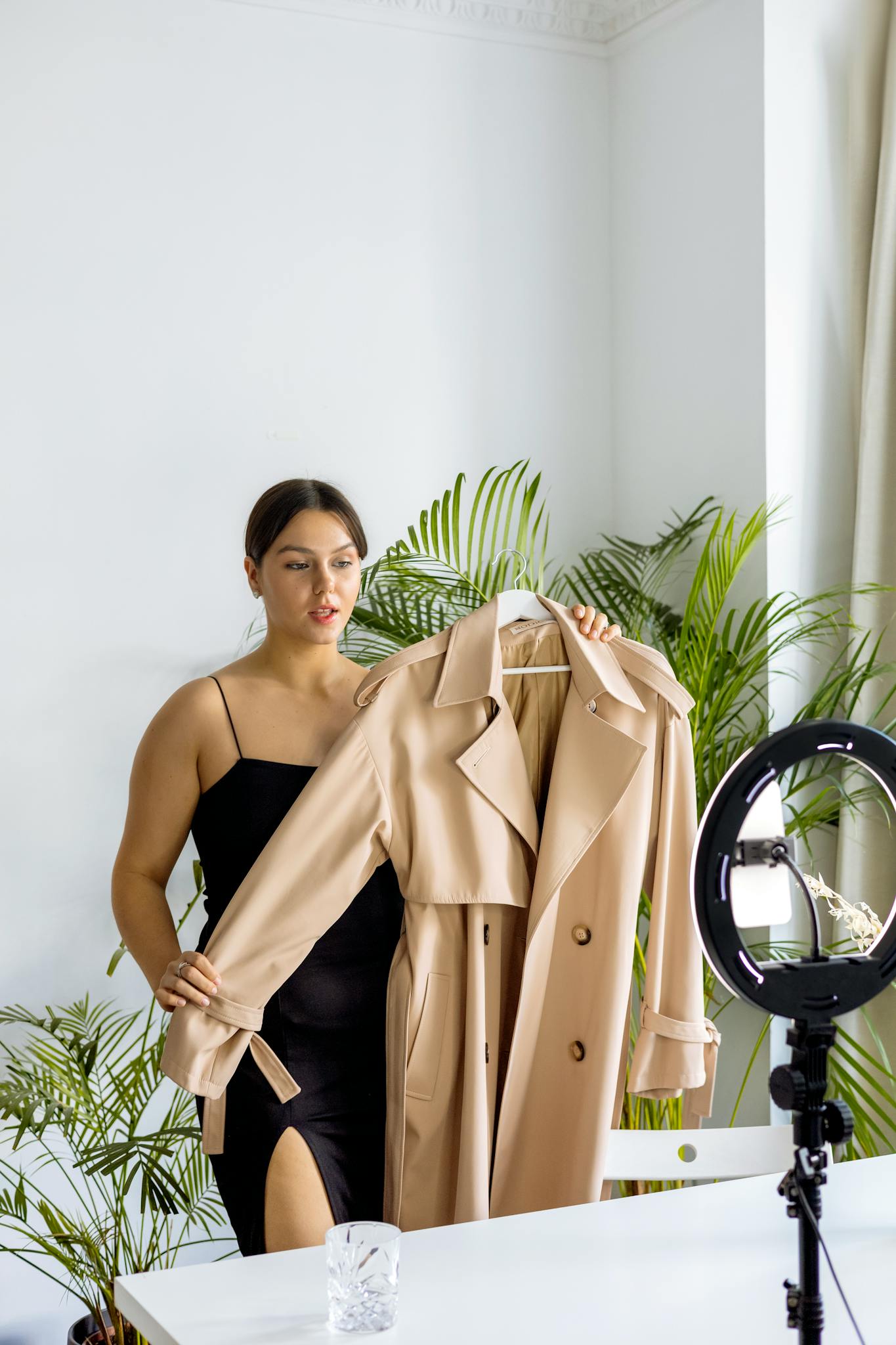 A fashionable woman vlogging about a stylish beige trench coat indoors.