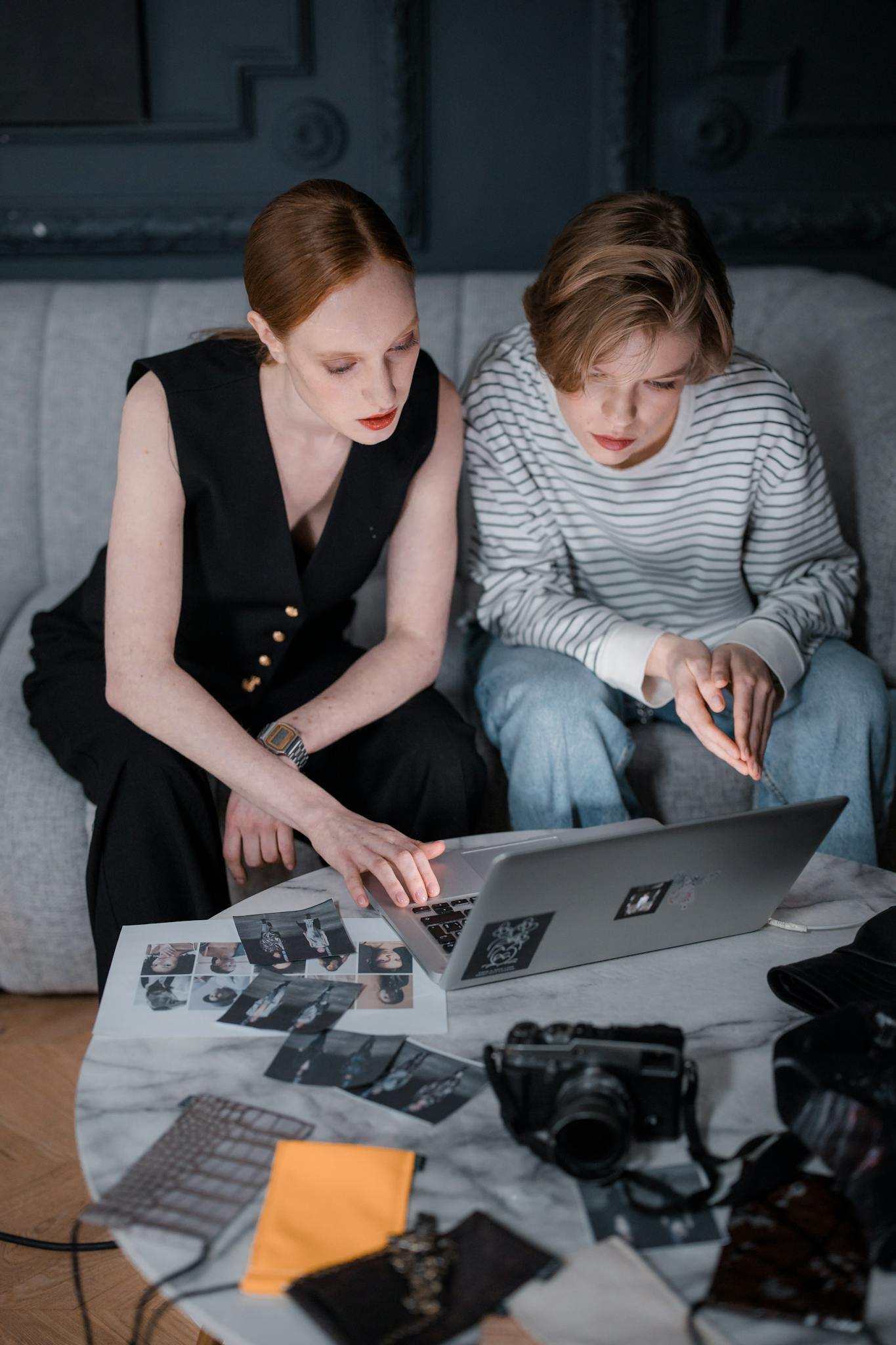 Two people working together on a creative project, reviewing photos on a laptop indoors.