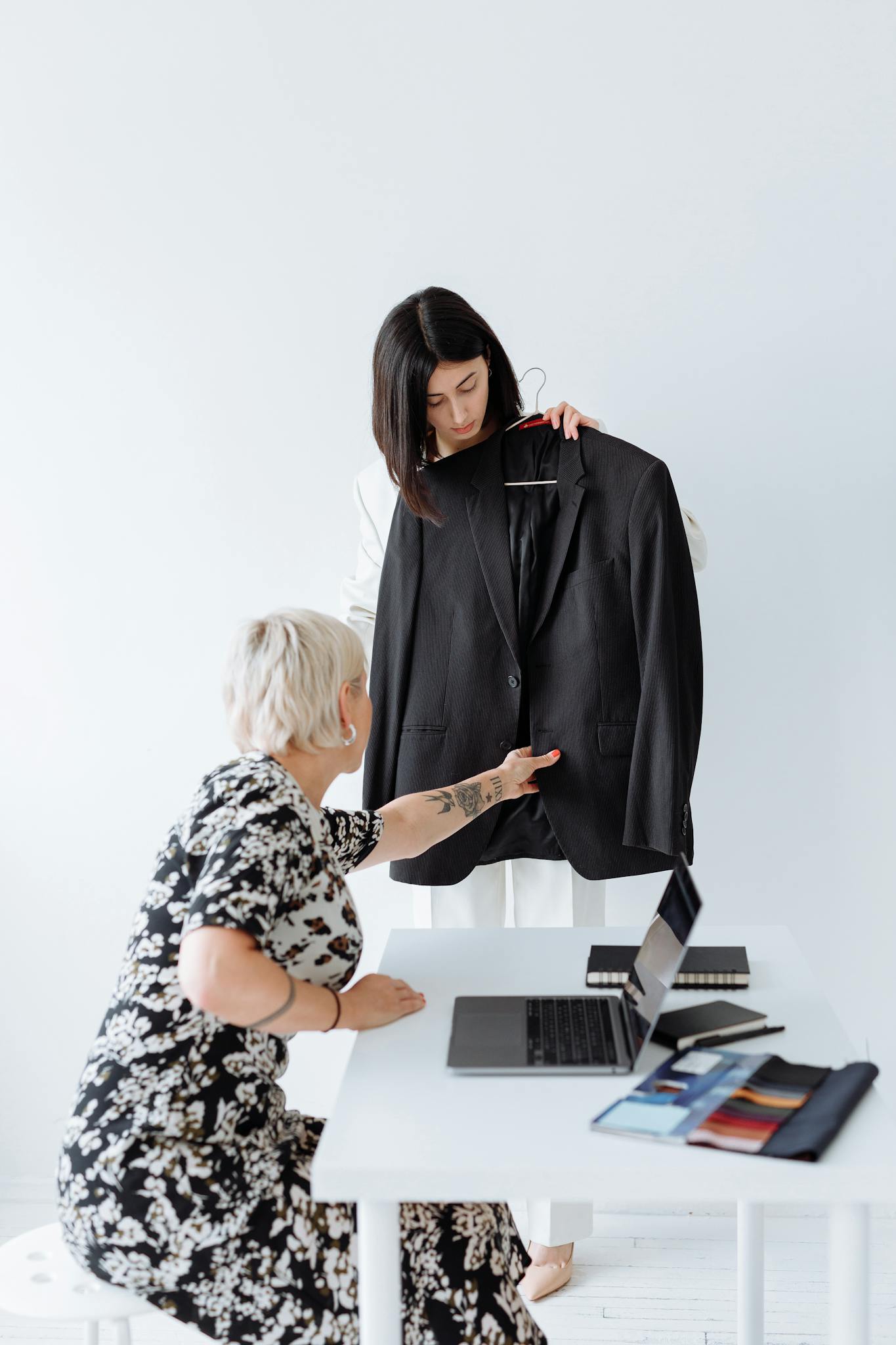 Two women discussing fashion choices with a suit in an office setting.